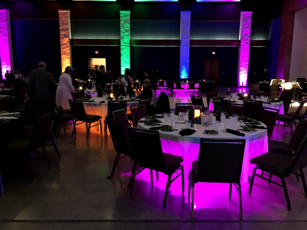 Pillars and tables lit in rainbow colors with led up-lights at a banquet.